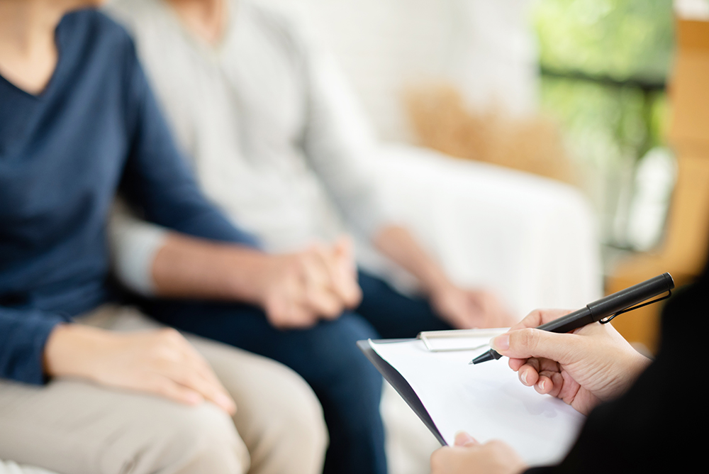 Young man and woman consulting with professional estate planning consultant. Couple sitting on sofa and holding hands together.